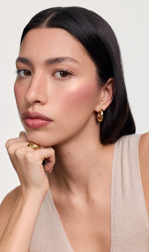 Model wearing makeup with gold earrings against a grey background.