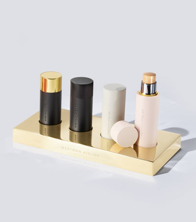 Four makeup products in a gold tray against a grey background.