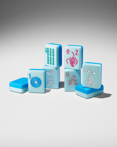 A set of miniature mahjong tiles arranged on a neutral gray gradient background. The tiles are light blue with white faces and multicolored Chinese characters and symbols.