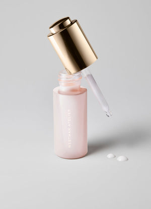 Pink skincare bottle with gold cap and dropper on a light gray background
