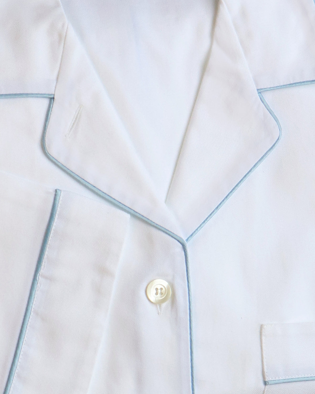 Close-up of white pajamas with blue piping and a button.
