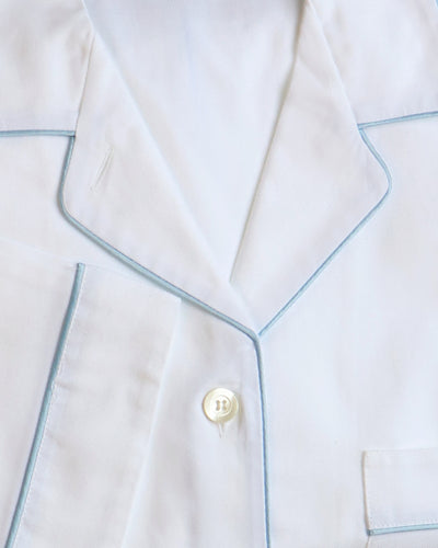 Close-up of white pajamas with blue piping and a button.
